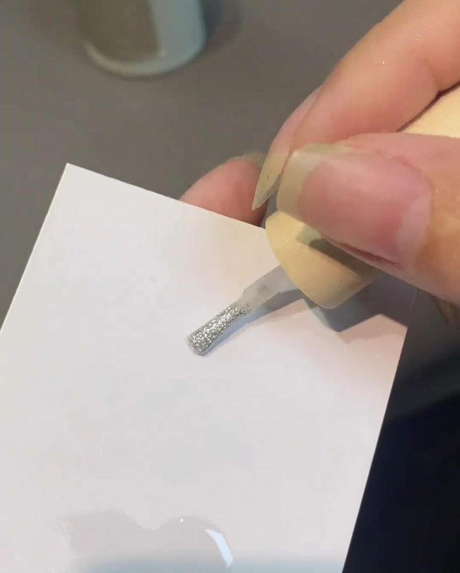 Un pincel mezclando top coat y polvo de perla sobre una paleta.