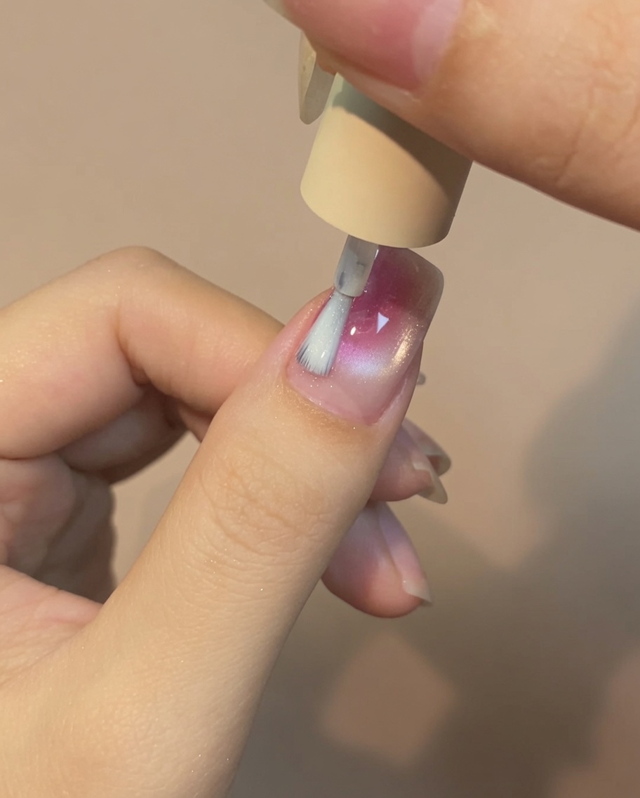 Un pincel aplicando una capa fina de top coat sobre la uña con diseño de rosa.