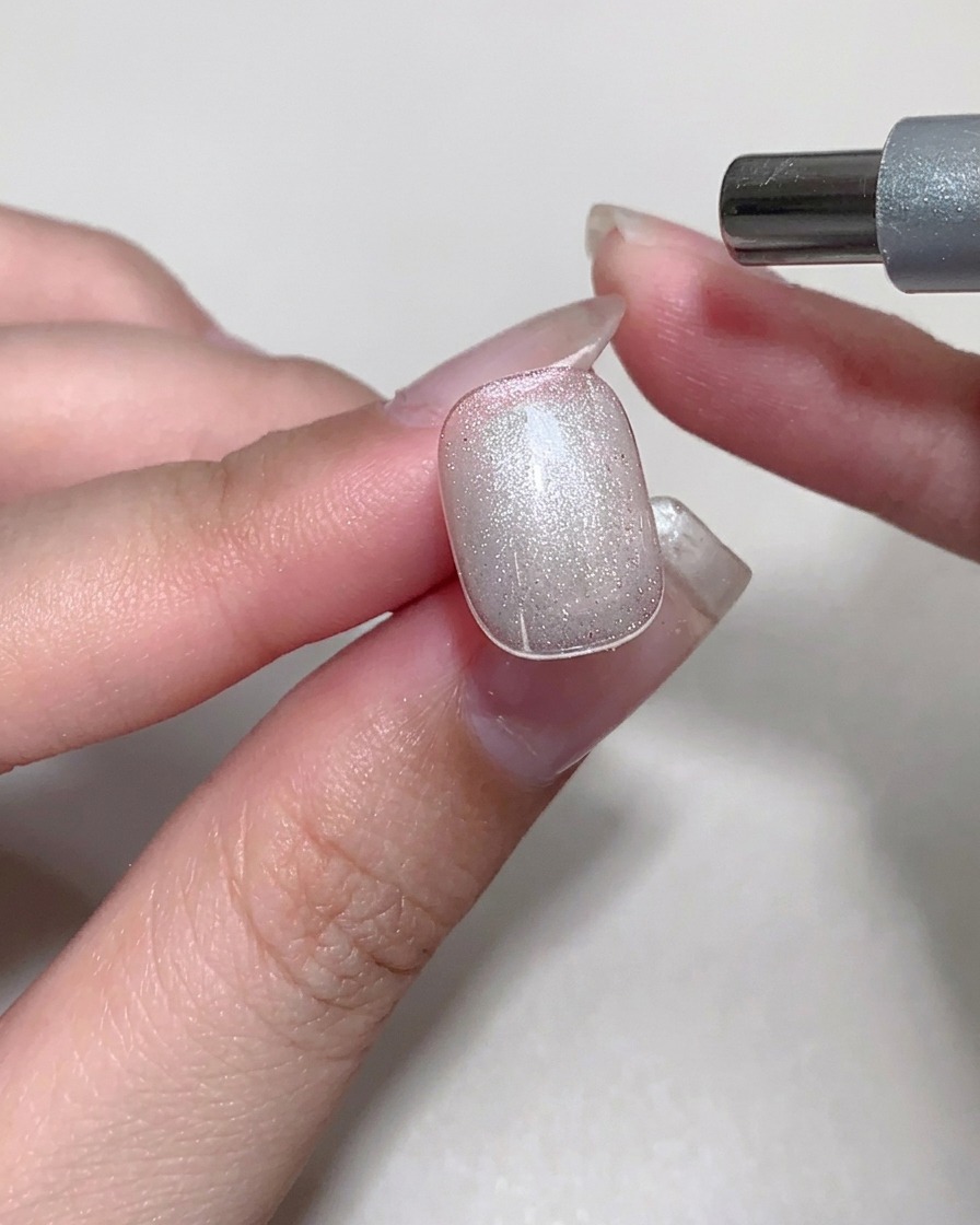 Un imán siendo utilizado sobre una uña con gel cat eye húmedo para crear un brillo similar al cristal.