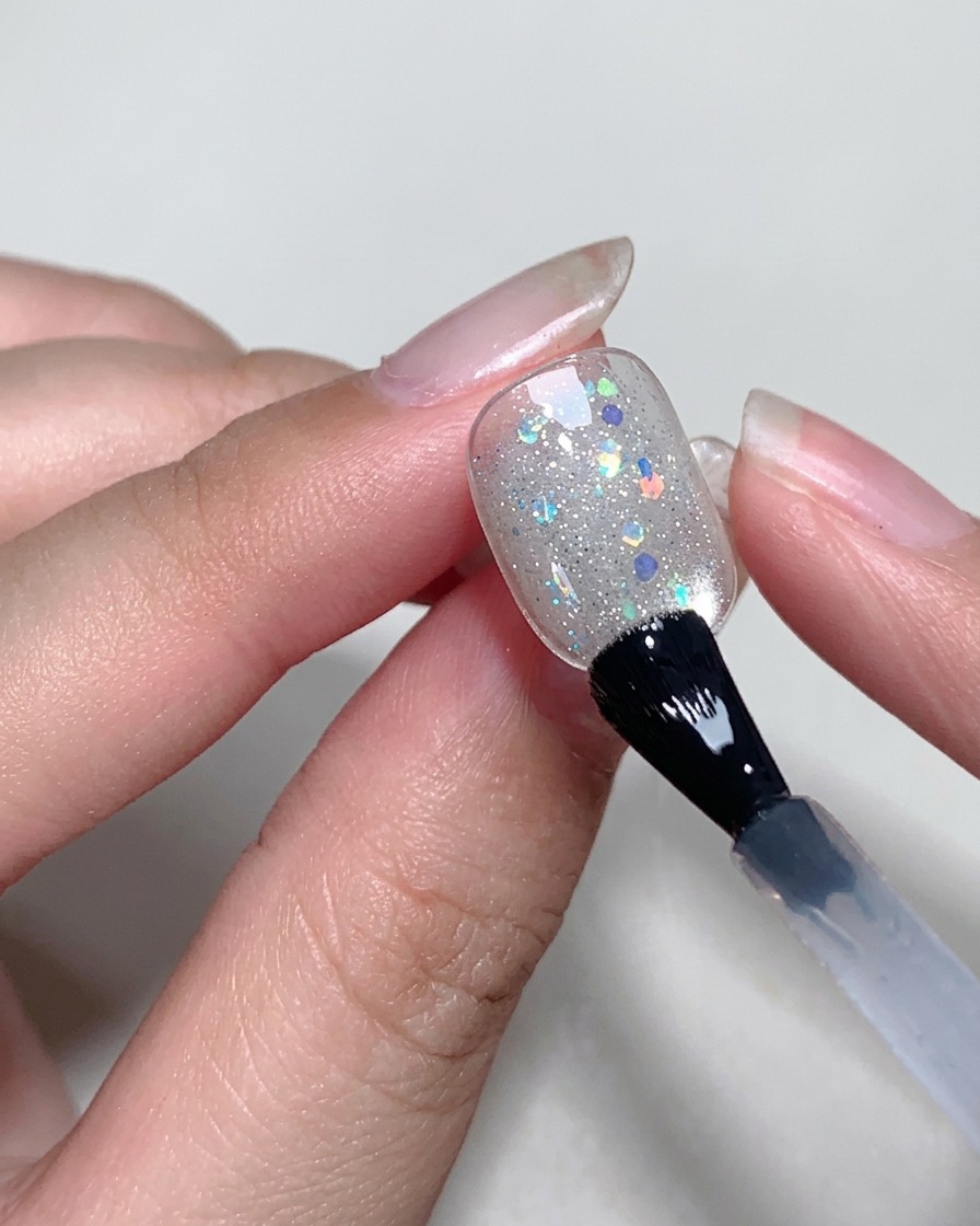 Aplicando una capa fina y transparente de blooming gel sobre la superficie de la uña usando un pincel.
