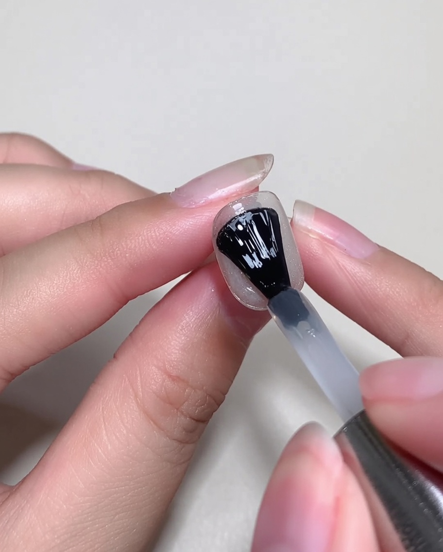 Un pincel de gel aplicando una capa fina de blooming gel transparente sobre una uña decorada.