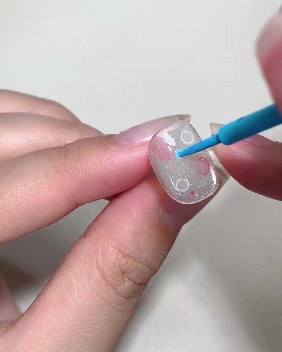 Una herramienta de punteado colocando pequeñas burbujas líquidas coloridas sobre la superficie de una uña.