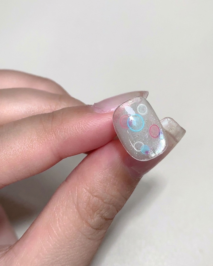 Un pincel aplicando un builder gel transparente y viscoso sobre una uña decorada.