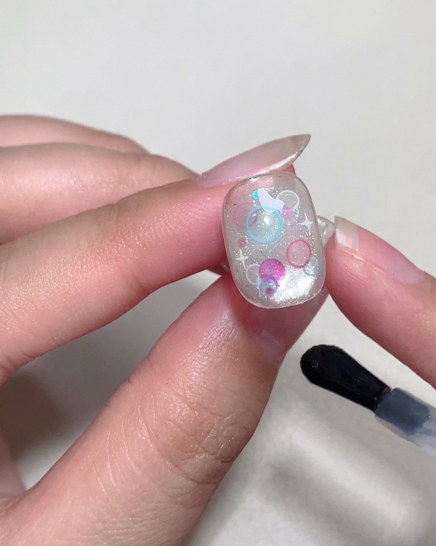 Un pincel aplicando un top coat brillante final sobre la superficie de la uña.