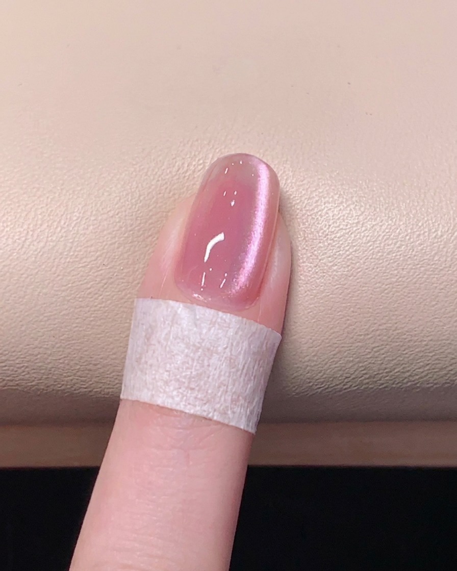 Un pincel aplicando una capa superior transparente y brillante sobre una uña de gel cat eye rosa.