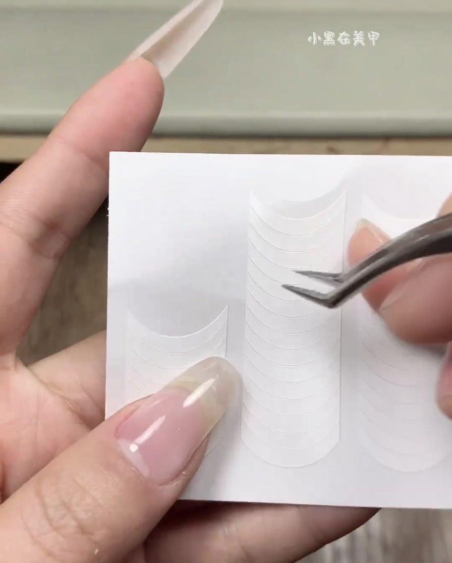 Una mano aplicando una pegatina blanca de guía francesa sobre una uña natural limpia.