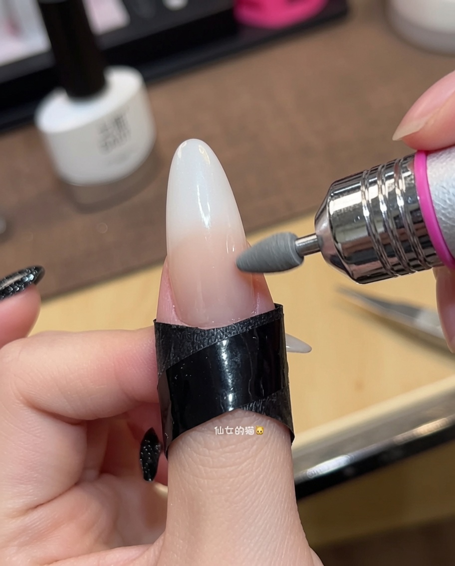 Primer plano de un pincel aplicando una segunda capa de esmalte de gel nude traslúcido sobre una uña.