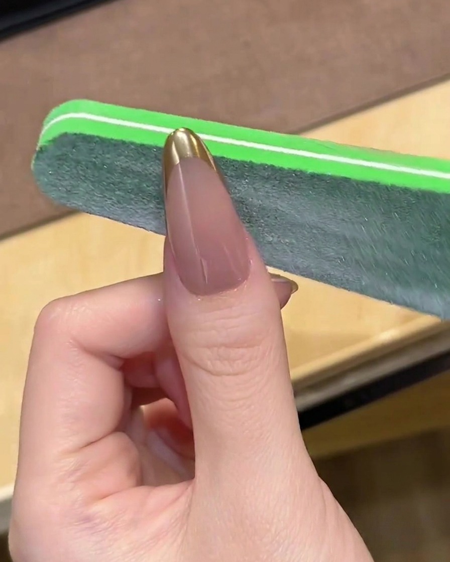 Una lima de uñas suavizando suavemente la punta de una manicura francesa cromada.