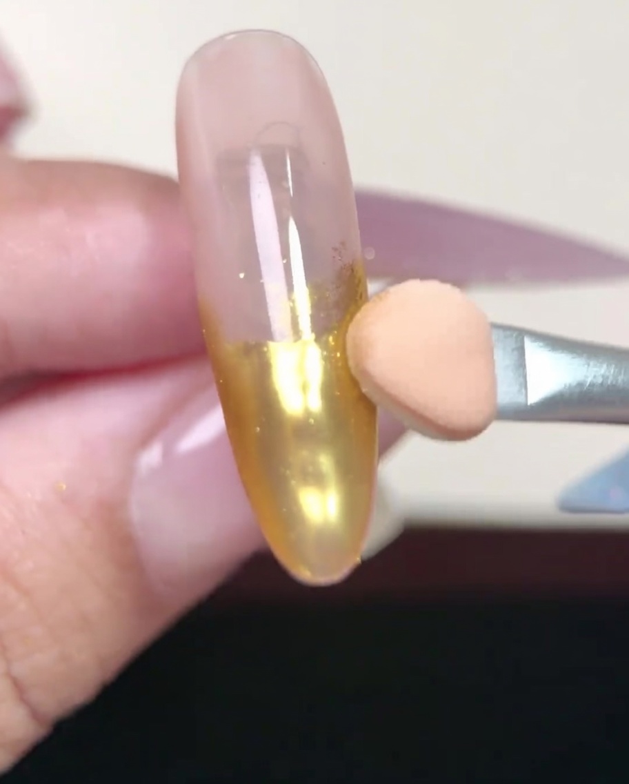 Pincel aplicando una capa de base gel nude sobre una uña almendrada preparada.