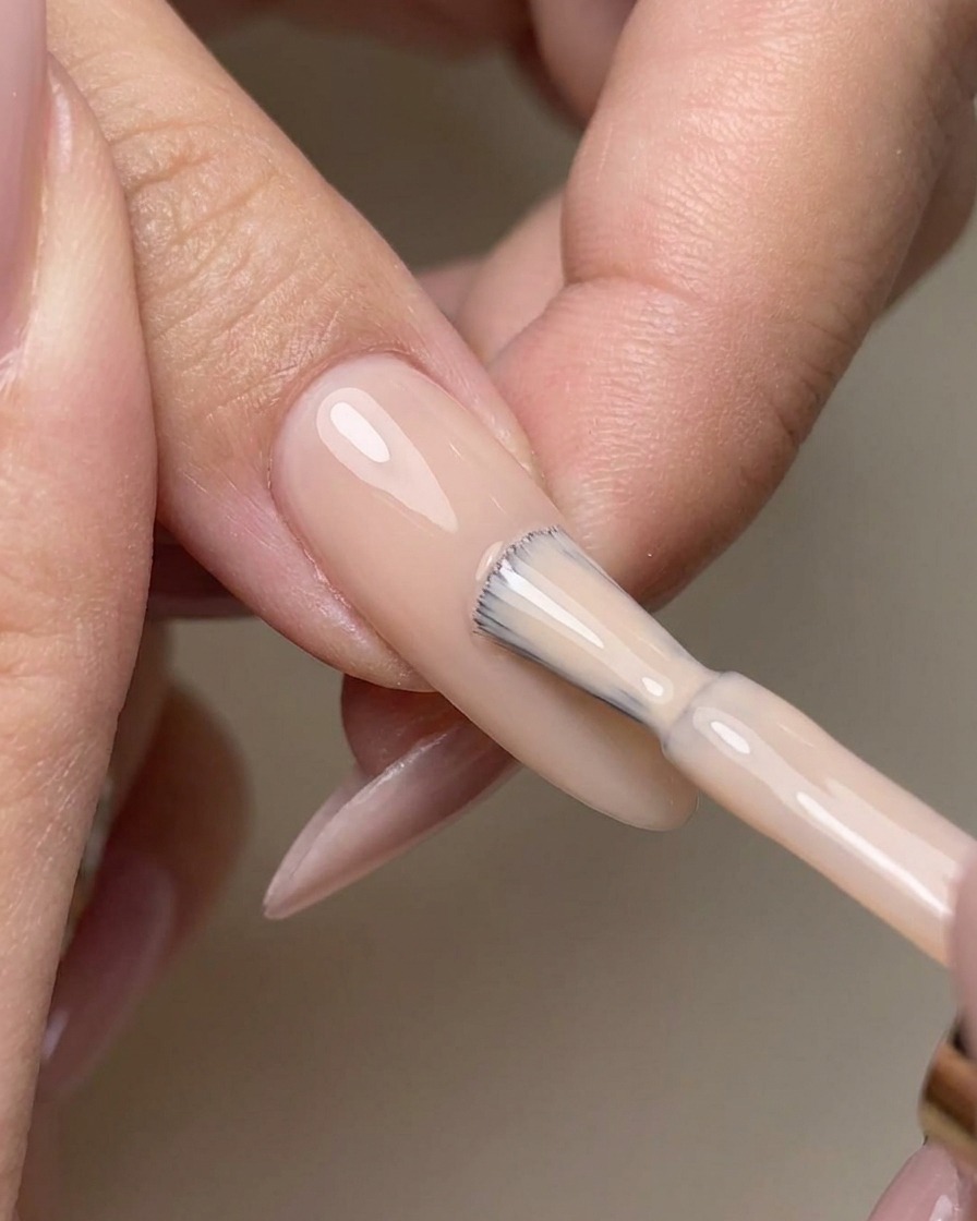 Pincel aplicando top coat sin capa de dispersión sobre la uña esmaltada en nude.