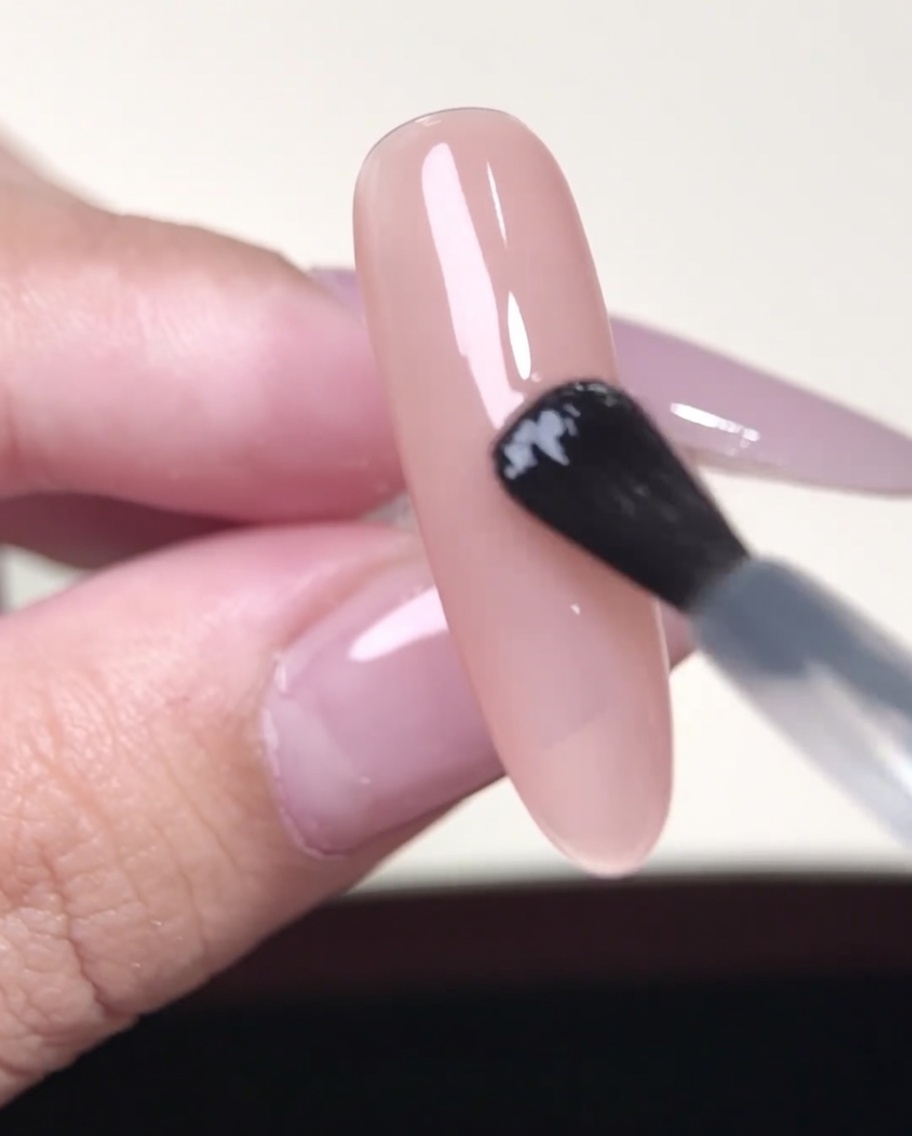 Pinzas colocando una pegatina para manicura francesa sobre una uña nude.