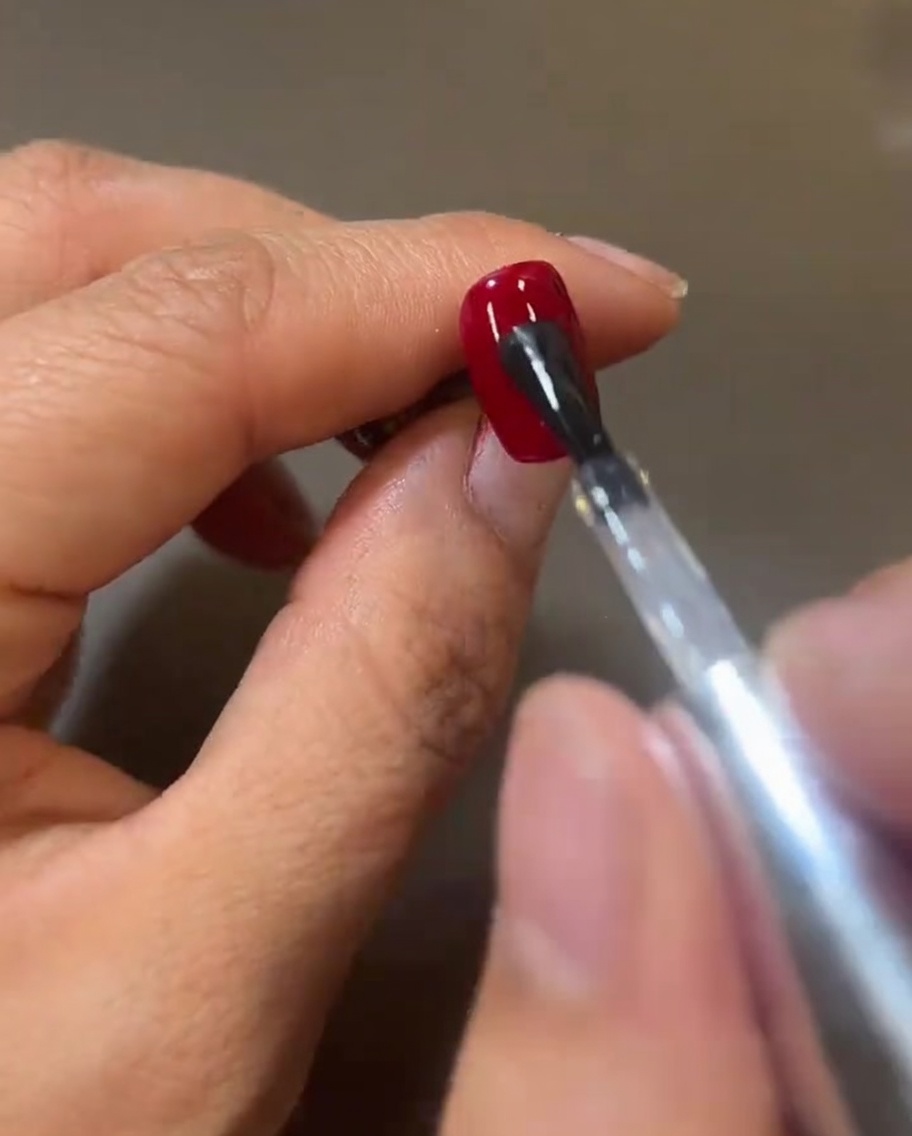 Un pincel aplicando una capa brillante de top coat transparente sobre el gel rojo, creando una superficie húmeda y reflectante.