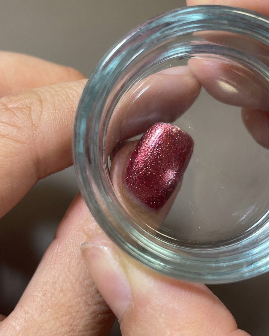 Primer plano de un estampador de silicona transparente presionando un diseño de comida blanco sobre una uña roja de textura aterciopelada.