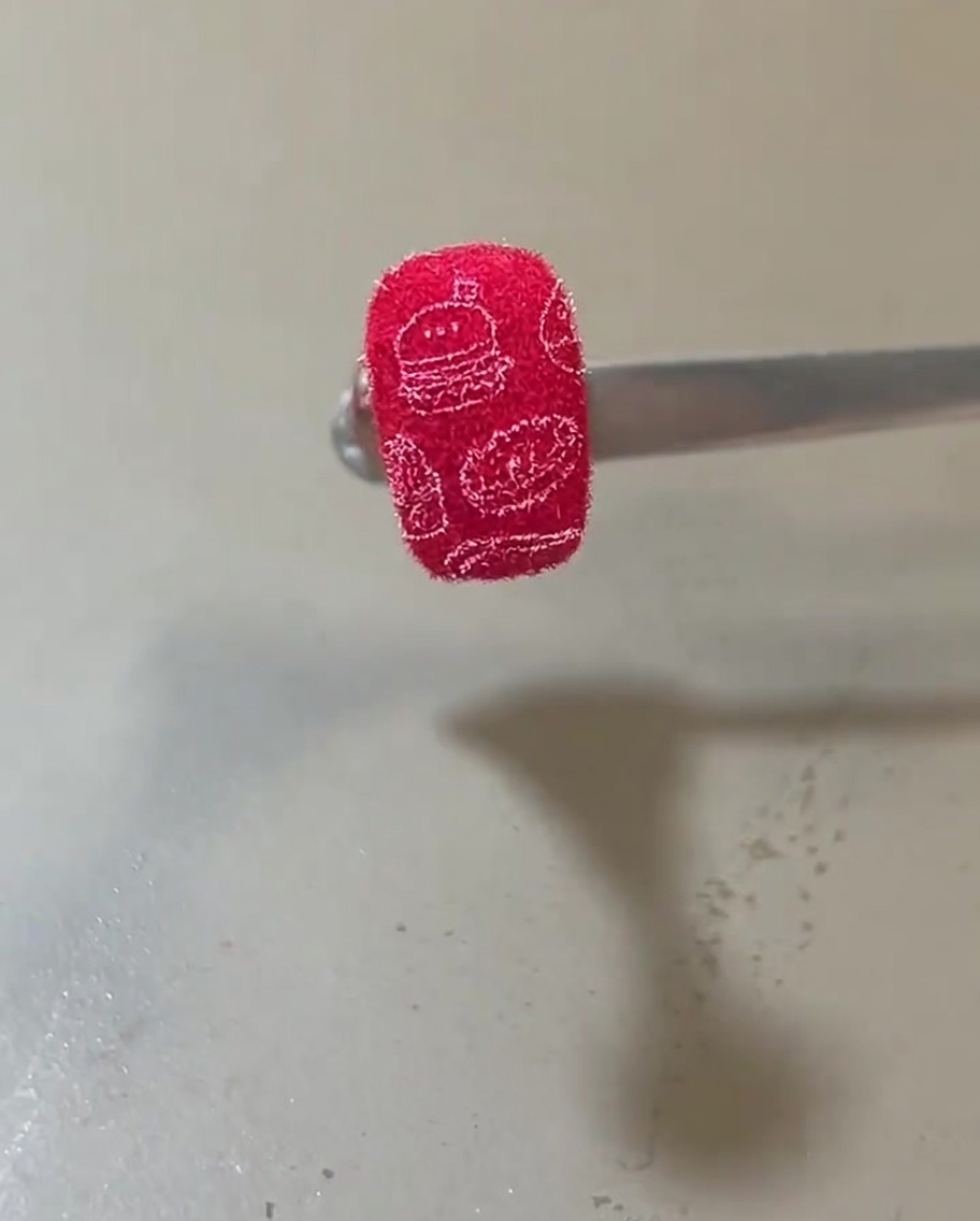 Una uña terminada con una textura aterciopelada roja vibrante adornada con ilustraciones blancas de hamburguesas y artículos de comida.