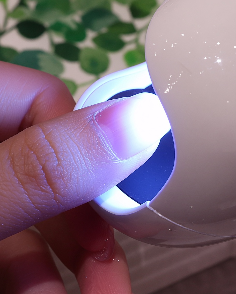 Uña con recubrimiento blanco texturizado bajo la luz púrpura de una lámpara UV/LED.