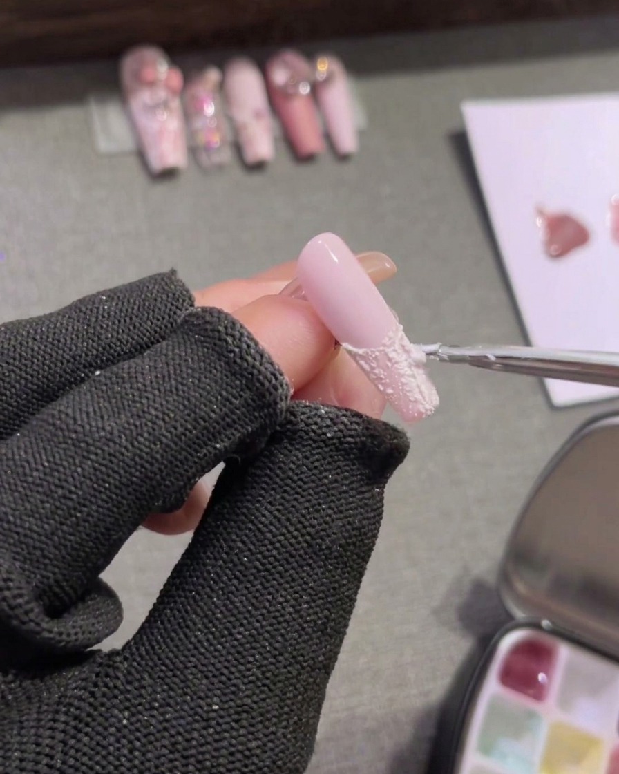 Un pincel de detalle rellenando la punta de una uña rosa con gel relieve blanco opaco.