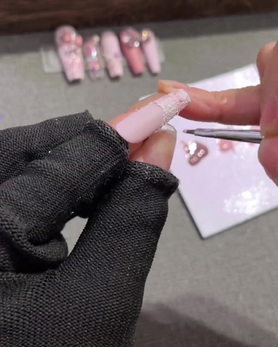 Un pincel de uñas fino dibujando líneas horizontales de color rosa claro a través de una punta blanca texturizada, cruzando líneas verticales para crear una cuadrícula.