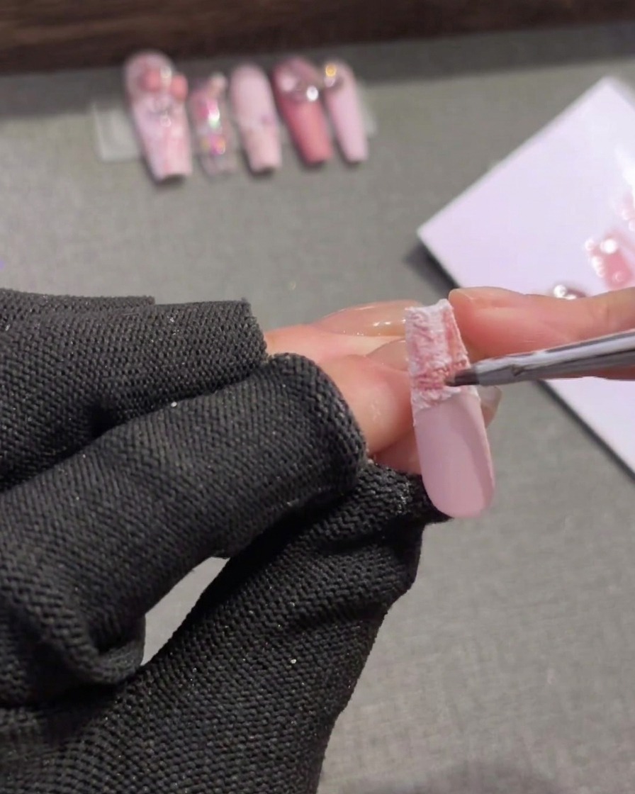 Un pincel fino aplicando un gel rosa de tono medio al borde superior de una punta de uña de cuadros para suavizar la transición.