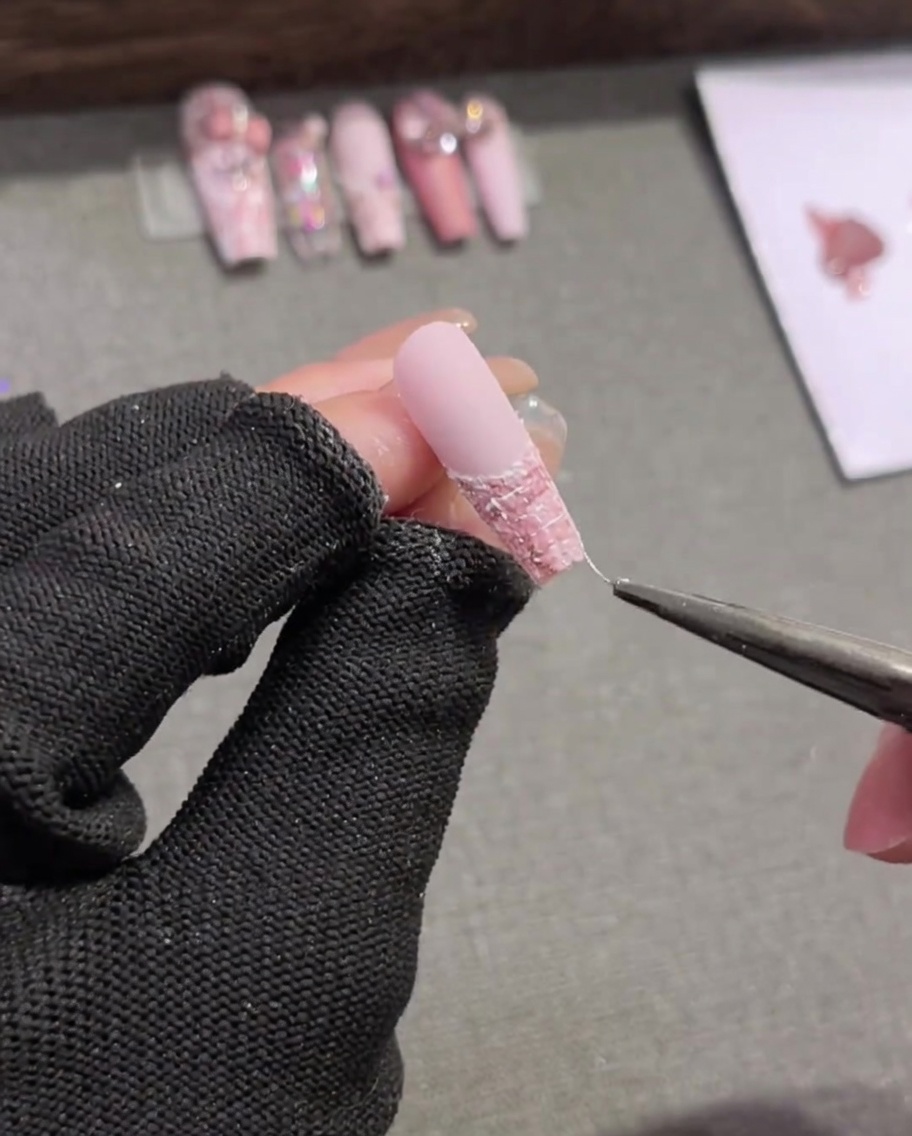 Un pincel liner dibujando cuidadosamente líneas horizontales blancas delgadas a través de un diseño de uñas de cuadros rosa y blanco.