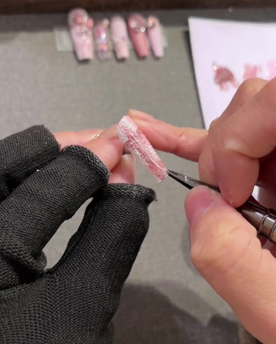 Una toma de primer plano de un pincel liner largo aplicando líneas blancas delgadas sobre un diseño de uñas de cuadros pintado.