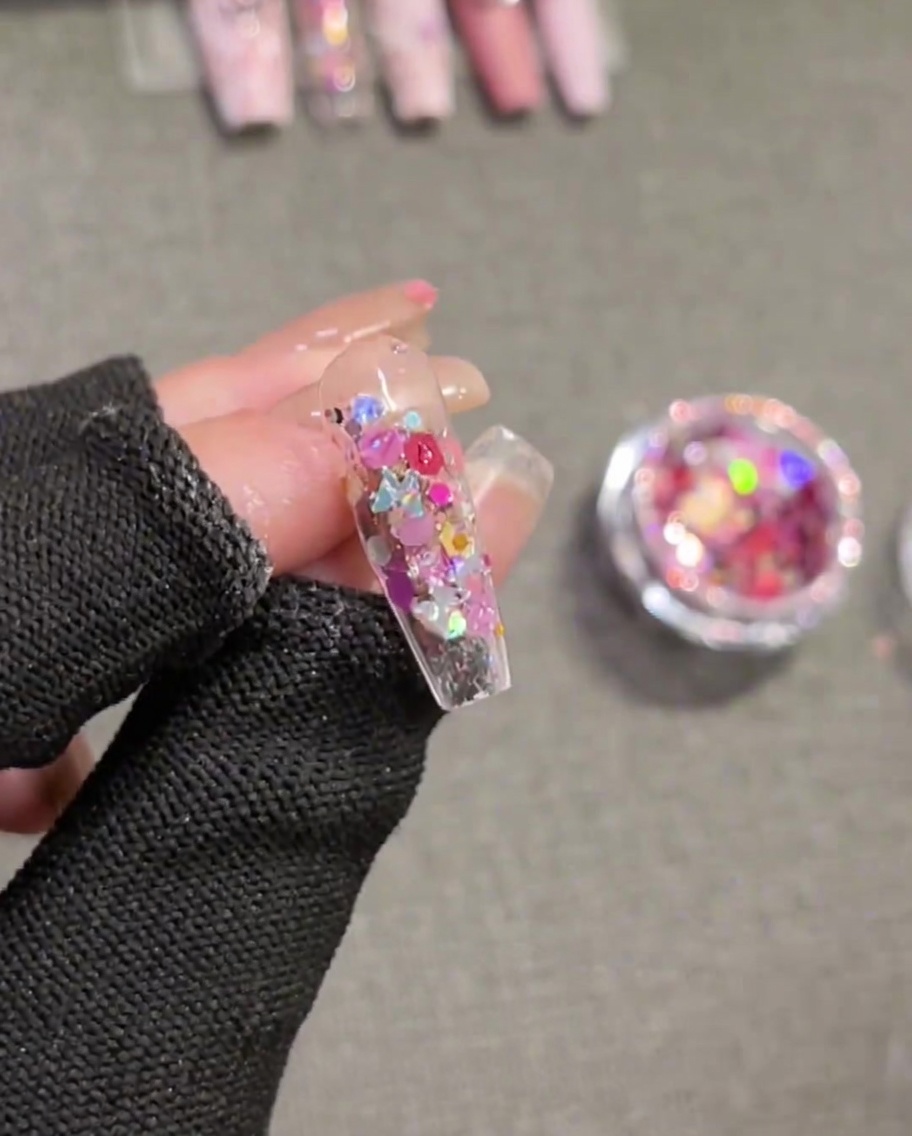 Un pincel aplicando un gel constructor de consistencia espesa y transparente sobre una uña decorada con lentejuelas, alisándola para crear una superficie nivelada.