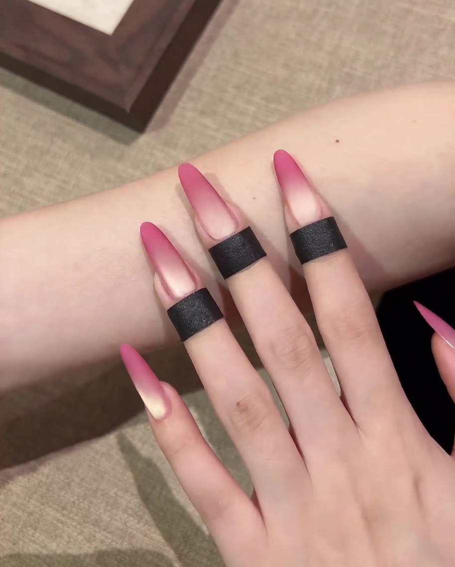 Primer plano de una esponja de maquillaje aplicando gel cat-eye rosa en la punta de la uña.