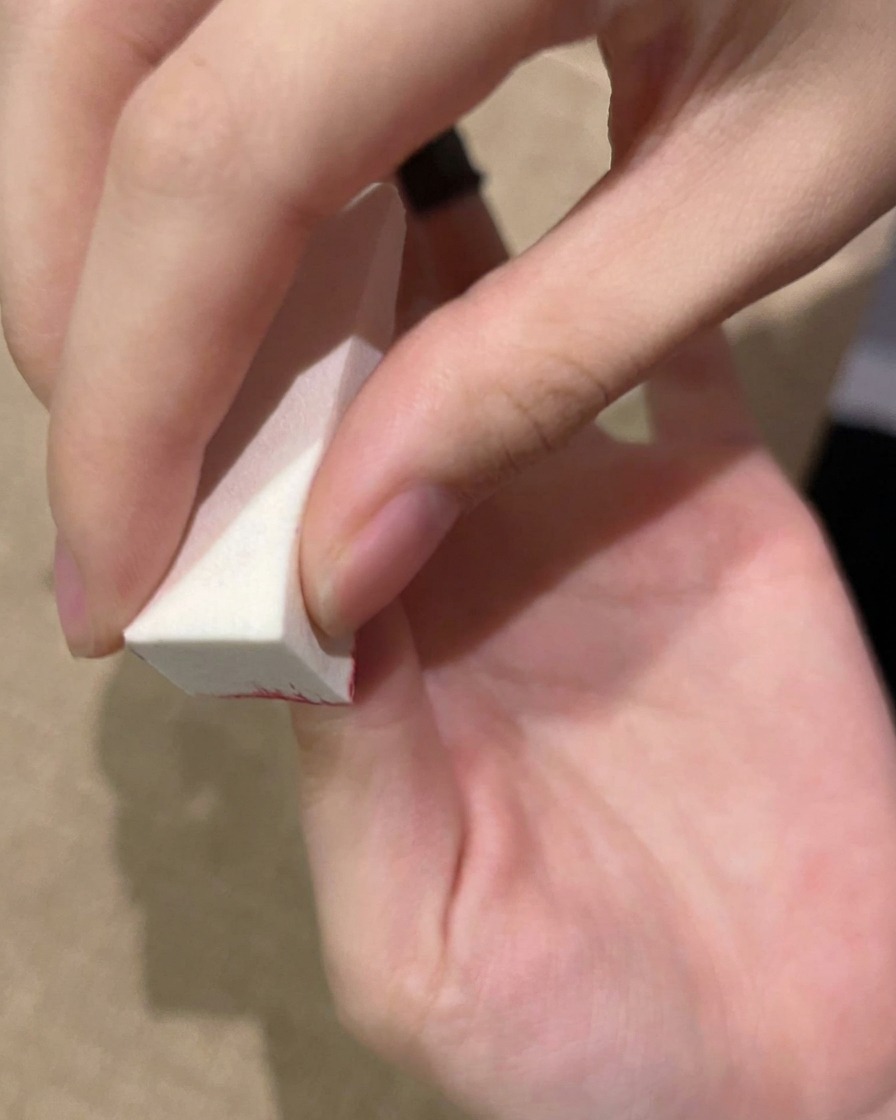 Una mano aplicando gel en la uña con una esponja antes de curar en la lámpara UV.