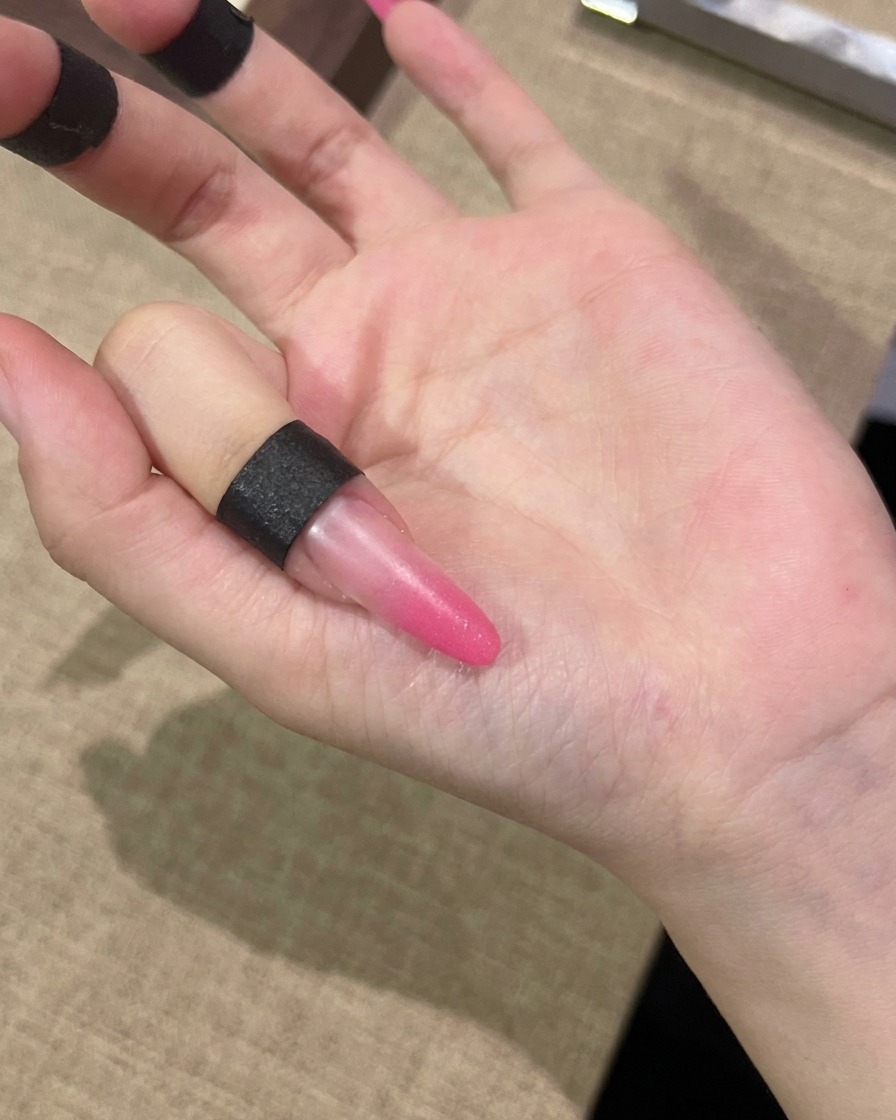 Un pincel aplicando una capa de gel cat-eye rosa sobre toda la superficie de la uña.