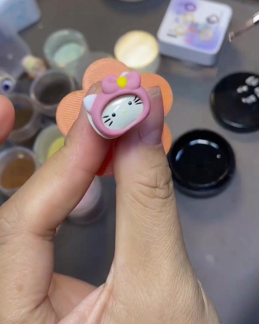 Un pincel fino para arte de uñas aplicando top coat transparente sobre un dije de uña 3D de Hello Kitty.