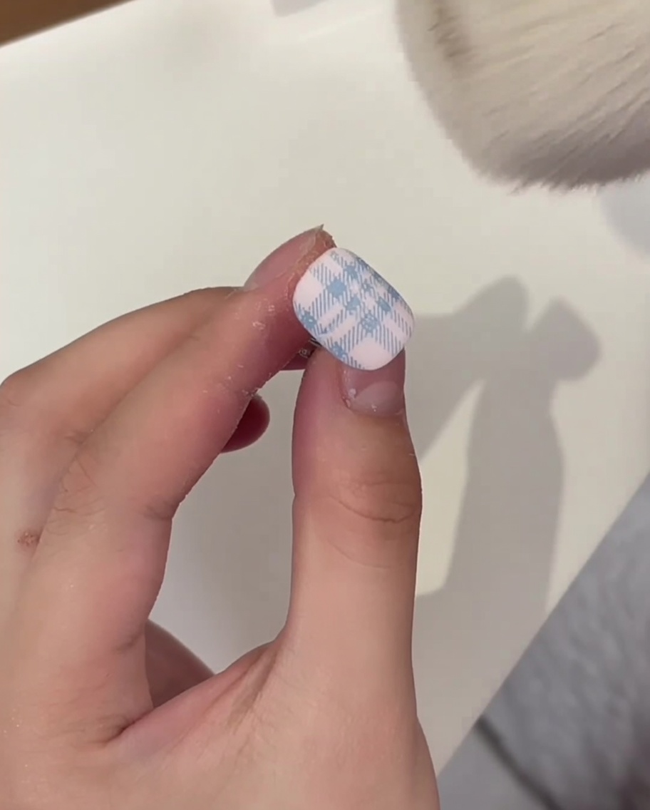 Una brocha de maquillaje esponjosa barriendo el exceso de polvo de cristal blanco de una uña curada con patrón de cuadros.