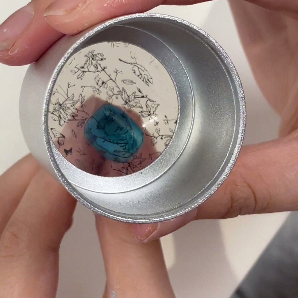 Un sello de silicona mantenido sobre una uña turquesa, mostrando el patrón floral negro posicionado para la transferencia.