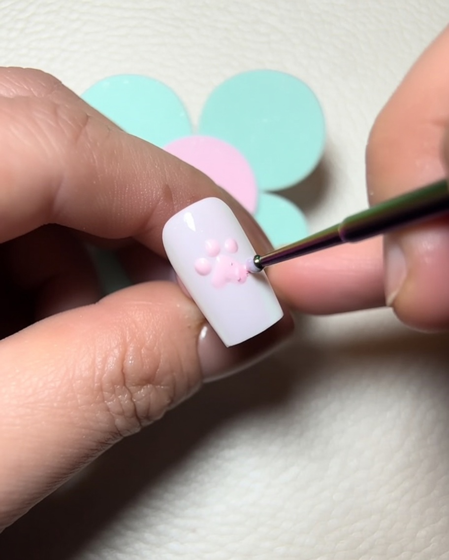 Un pincel de detalle aplicando gel de escultura transparente sobre los dedos rosas para añadir dimensión.