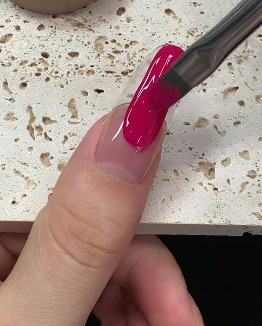 El pincel suavizando el esmalte de gel magenta para asegurar una cobertura completa y uniforme en la uña.