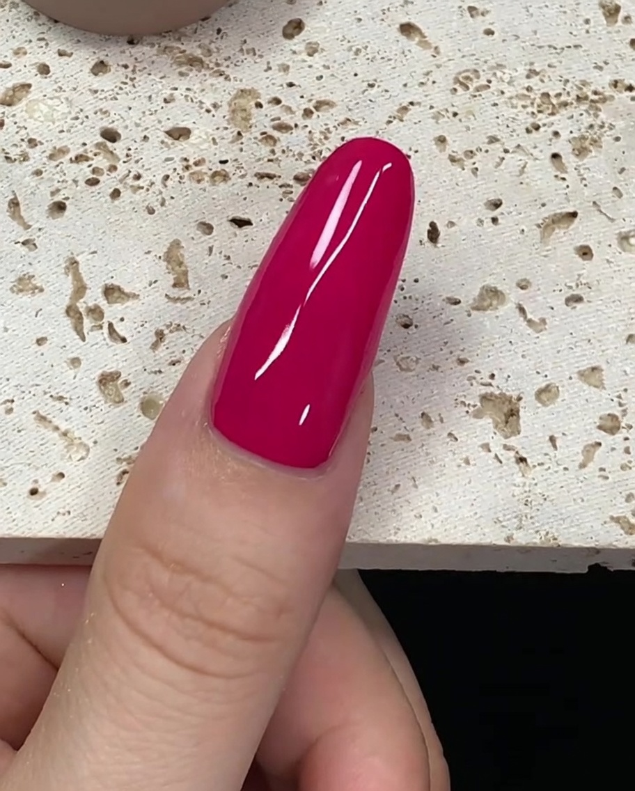 Un pincel cargado con esmalte de gel rojo intenso cerca de la cutícula de una uña.