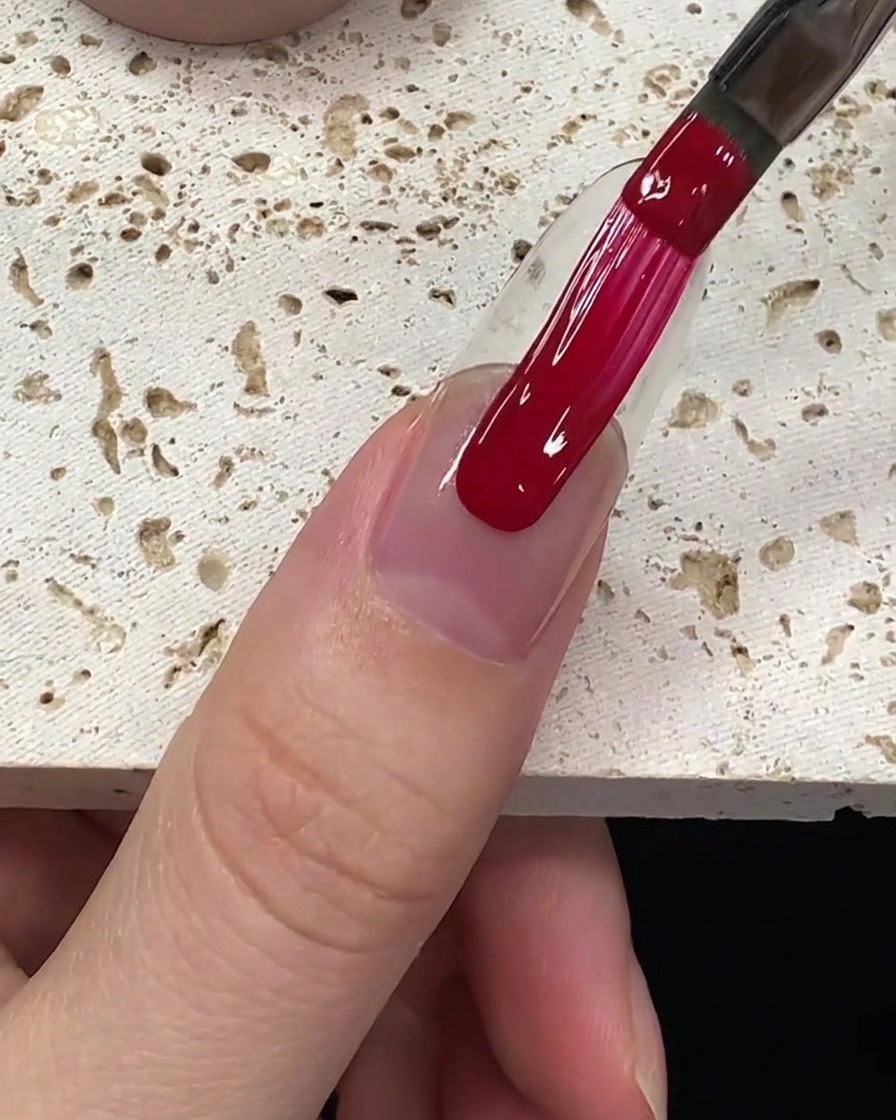 Una aplicación suave de esmalte de gel rojo intenso siendo arrastrado por la placa ungueal.