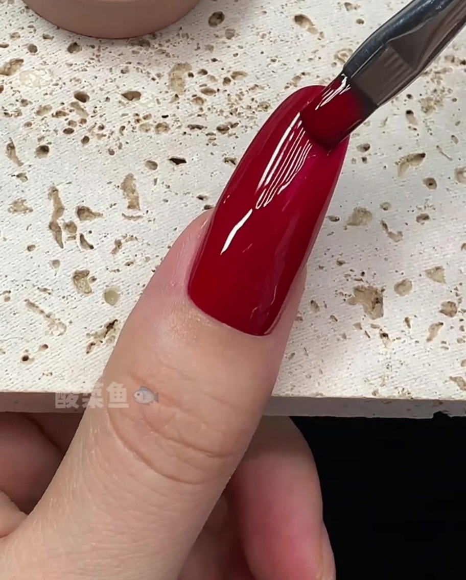 Vista cercana de un pincel perfeccionando los bordes de una uña recubierta con esmalte de gel rojo intenso.