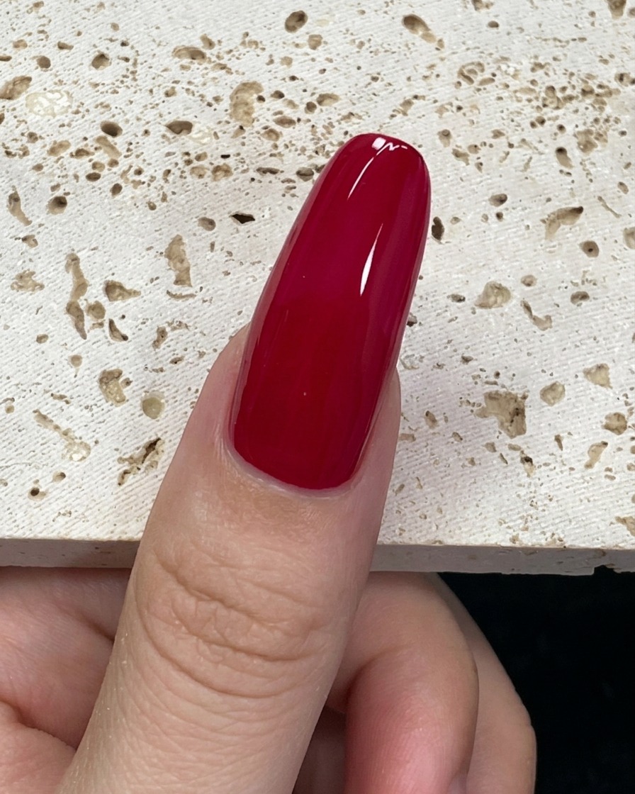 Vista cercana de un pincel de uñas cargado con esmalte de gel verde menta posicionado en la base de la uña.