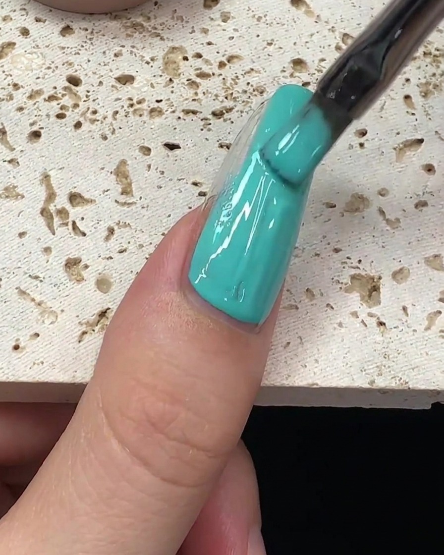 Una pincelada de esmalte de gel verde menta siendo arrastrado por el centro de la uña.