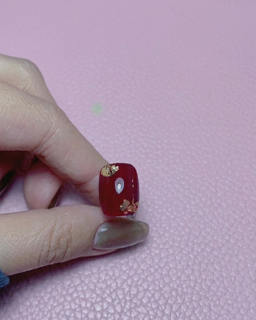 Primer plano de una uña roja con detalles de pan de oro, cubierta con un top coat de alto brillo.