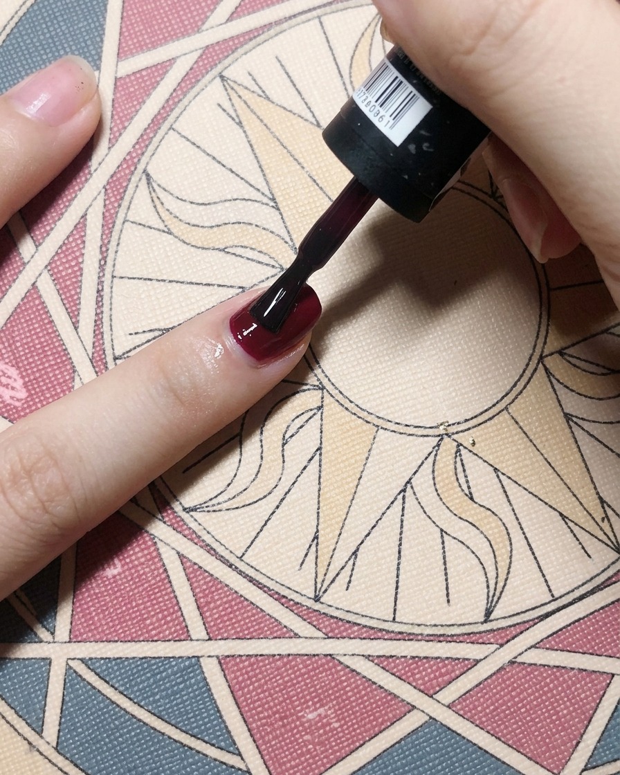 Un pincel aplicando un esmalte de gel rojo burdeos sobre la capa base de la uña, creando un color sólido y opaco.