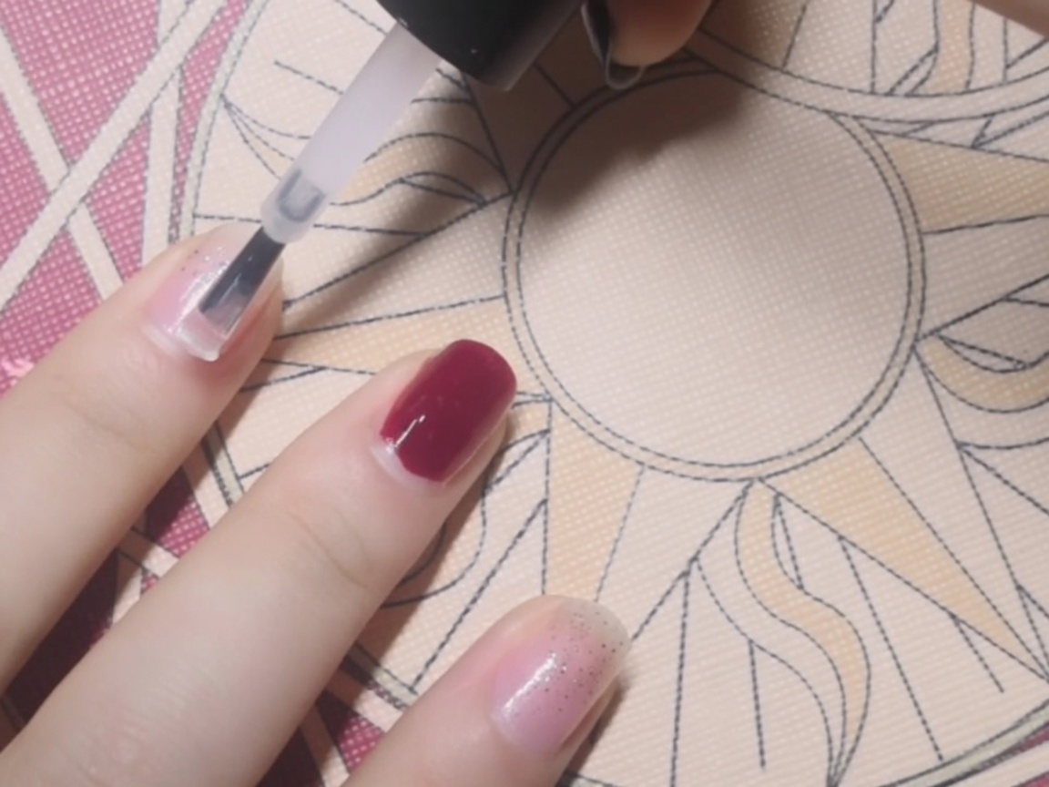 Primer plano de una base coat transparente aplicándose con un pincel sobre una uña.