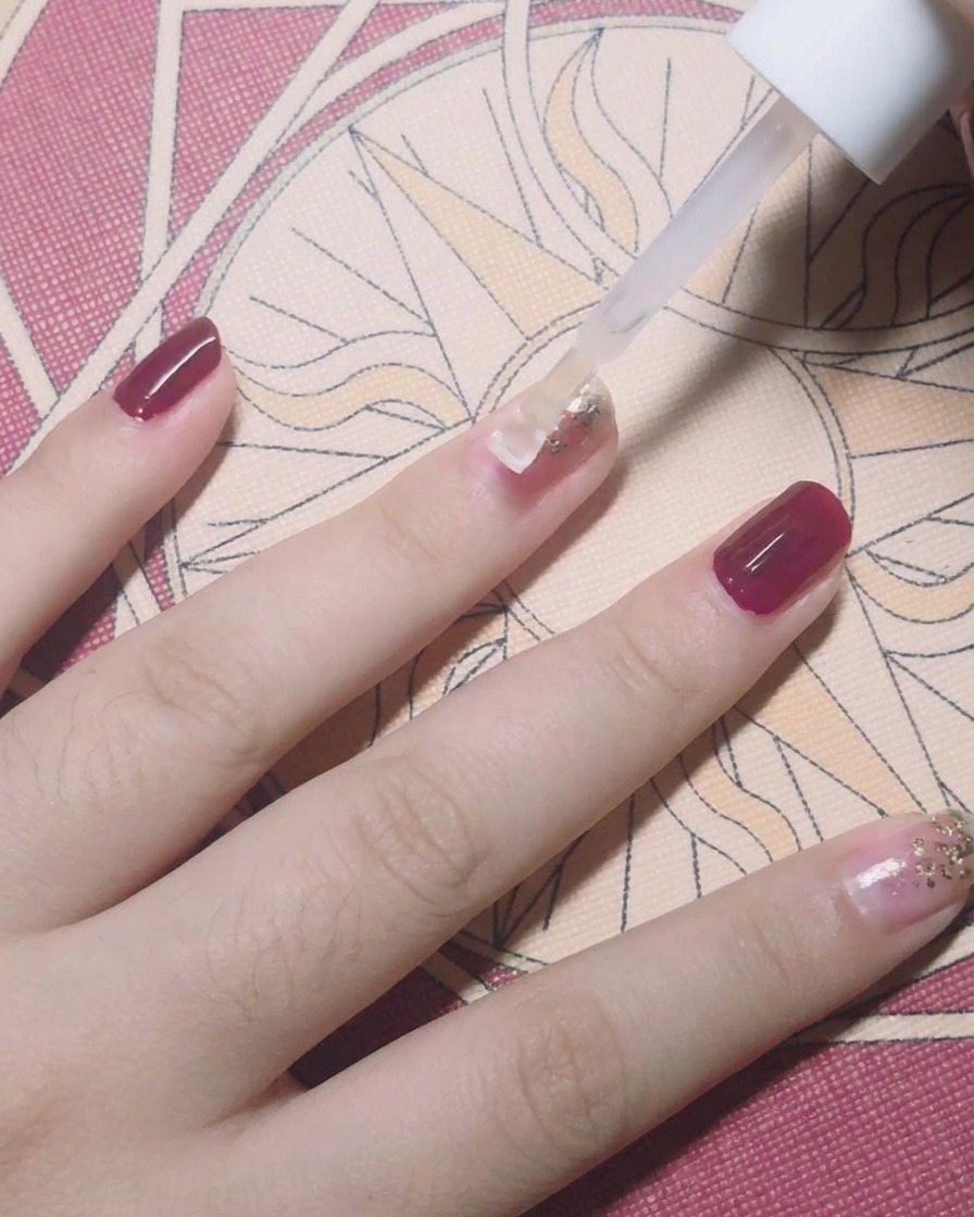 Un pincel aplicando un top coat transparente sobre una uña decorada con pan de oro.