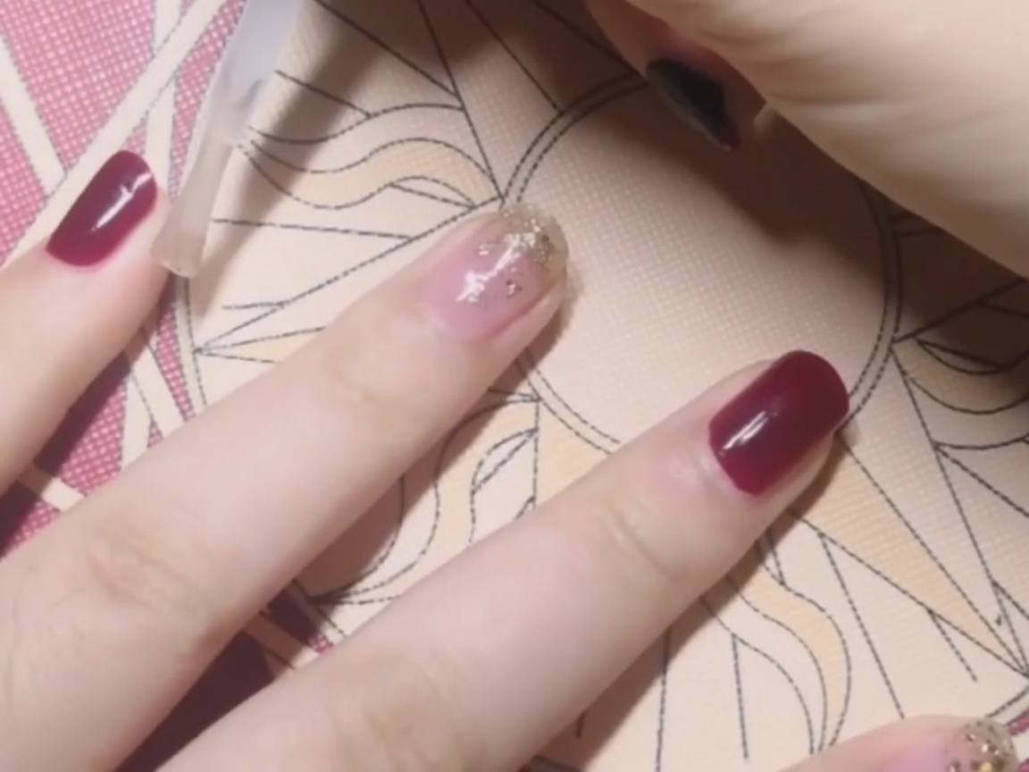 Un top coat transparente aplicándose sobre una uña roja sólida.