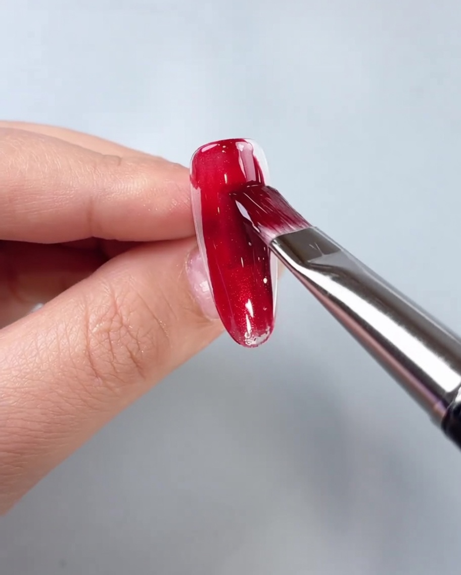 Un pincel aplicando gel ojo de gato rojo en el centro de un tip transparente.