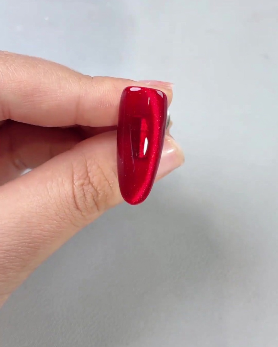Un top coat brillante aplicado sobre una uña magnética roja terminada, mostrando mucho brillo.