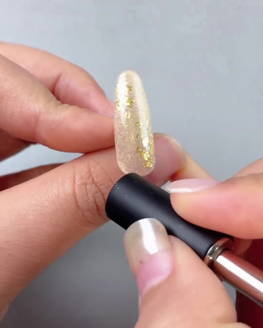 Un imán para uñas colocado cerca de una uña pintada con gel dorado para crear una línea ojo de gato reflectante.