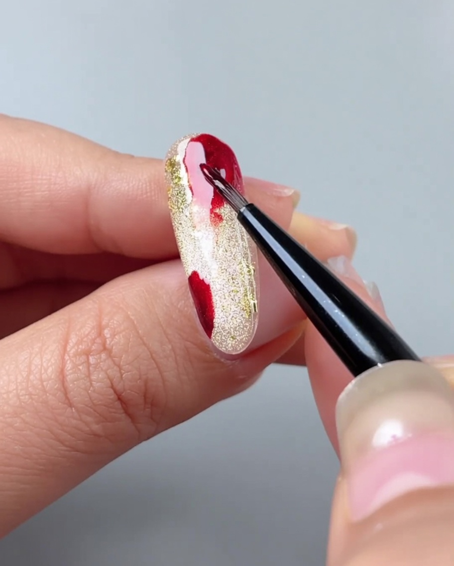 Un pincel difuminando parches de gel rojo en un degradado usando gel acuarela.