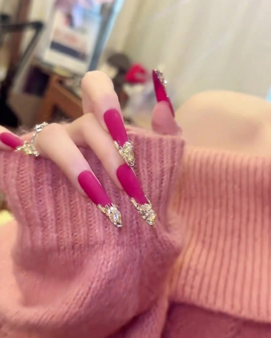 Una mano con un suéter rosa suave moviéndose ligeramente para mostrar el largo y la curvatura de las uñas almendradas largas de color rosa mate.
