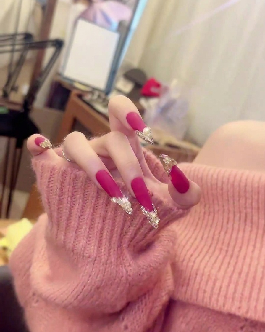 Un plano cerrado y nítido de un solo dedo que muestra la ubicación exacta de los racimos de cristales sobre el esmalte rosa fucsia mate.