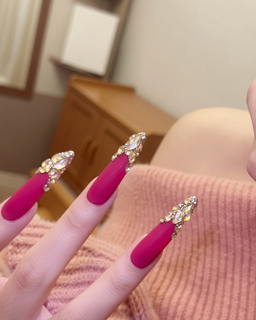 Un ángulo cercano de las uñas enfocado específicamente en los brillantes arreglos de cristales colocados en la base de las uñas rosas mate.